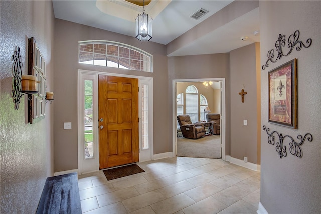 entryway with visible vents, baseboards, a high ceiling, a tray ceiling, and light tile patterned floors