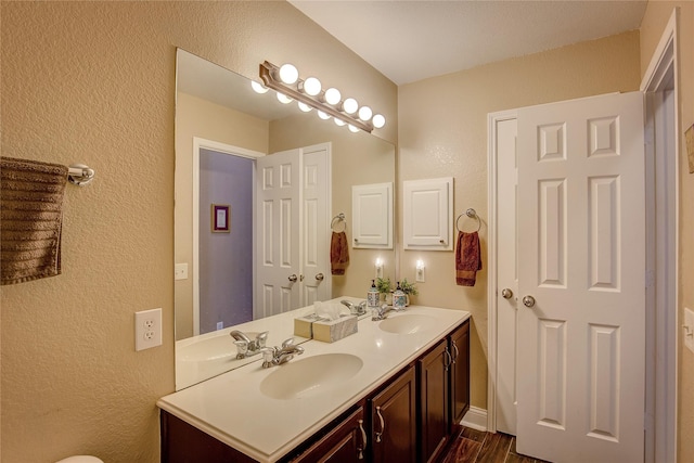 full bath with double vanity, a textured wall, a sink, and wood finished floors