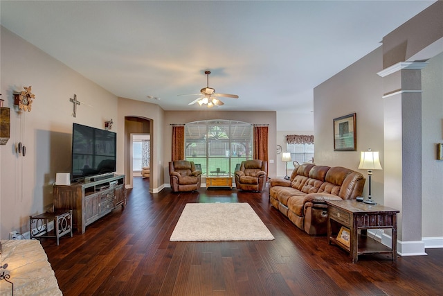 living room featuring baseboards, a ceiling fan, dark wood finished floors, and arched walkways