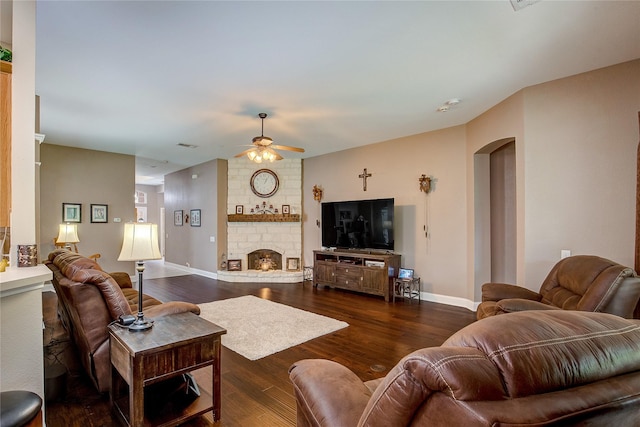 living room featuring baseboards, dark wood-style floors, arched walkways, a large fireplace, and a ceiling fan