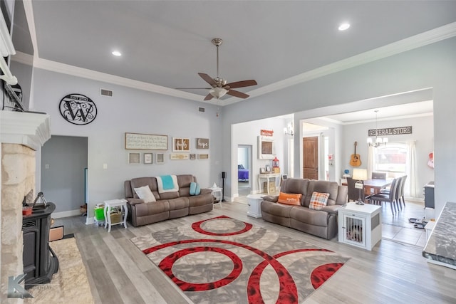 living room with a wood stove, ceiling fan with notable chandelier, light wood-type flooring, visible vents, and ornamental molding