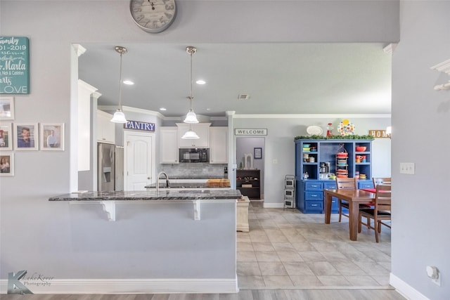 kitchen with white cabinets, black microwave, a kitchen breakfast bar, dark stone counters, and ornamental molding