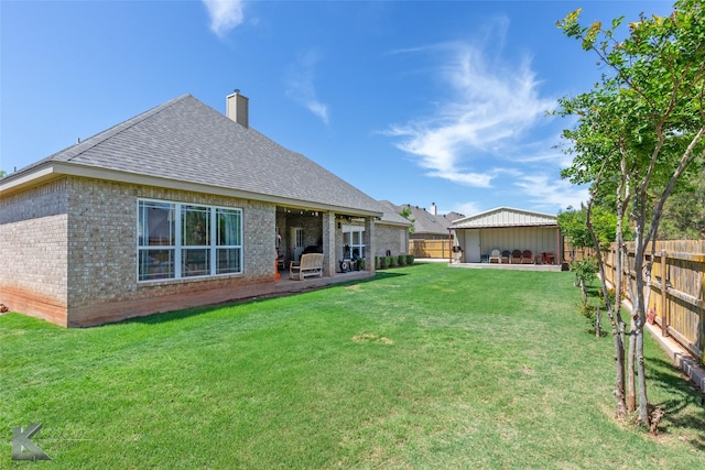 back of house with a fenced backyard, a chimney, brick siding, a shingled roof, and a yard