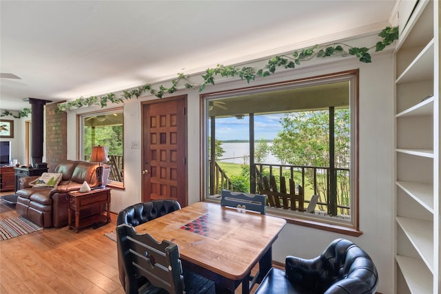 dining room featuring a water view, plenty of natural light, decorative columns, and light wood-type flooring