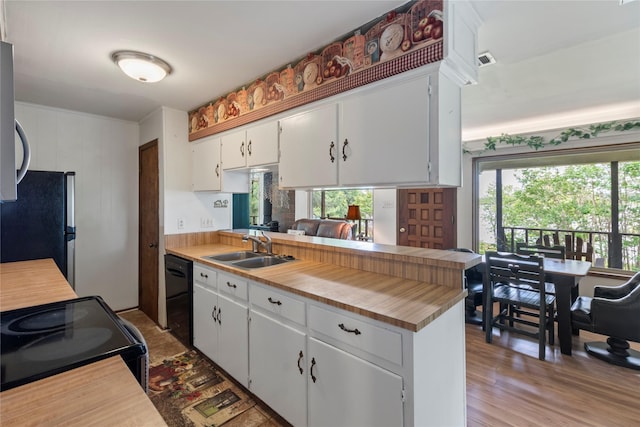 kitchen with a peninsula, light wood-type flooring, white cabinetry, a sink, and black appliances