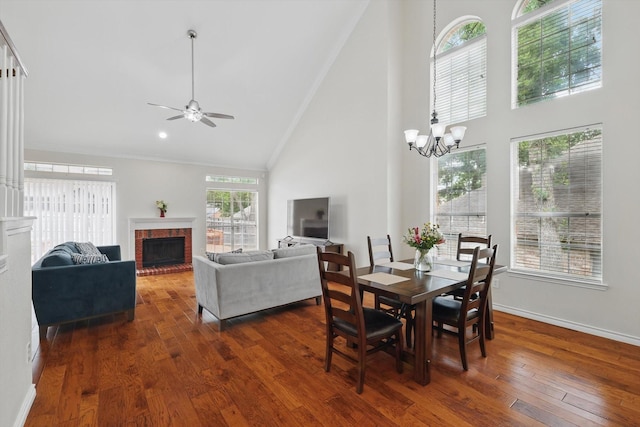 dining area with a brick fireplace, high vaulted ceiling, ceiling fan with notable chandelier, baseboards, and dark wood-type flooring