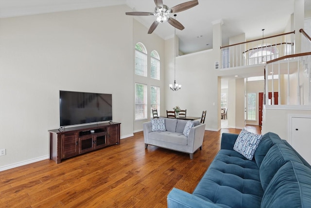 living room with visible vents, a towering ceiling, wood finished floors, baseboards, and ceiling fan with notable chandelier