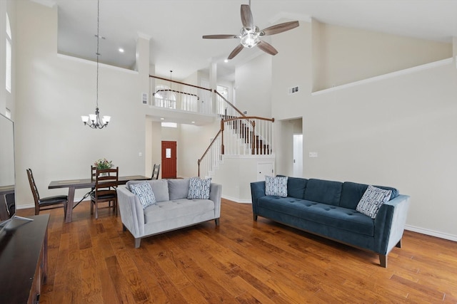 living area with high vaulted ceiling, ceiling fan with notable chandelier, stairs, wood finished floors, and visible vents