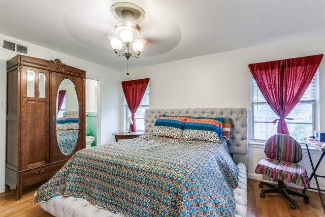 bedroom featuring multiple windows, ensuite bath, wood finished floors, and visible vents