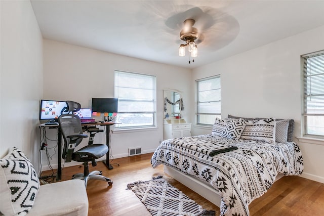 bedroom with a ceiling fan, baseboards, visible vents, and wood finished floors