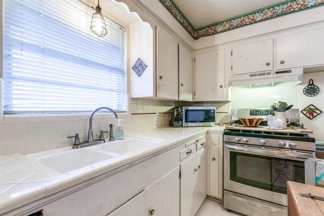 kitchen with under cabinet range hood, stainless steel appliances, tile countertops, and a sink