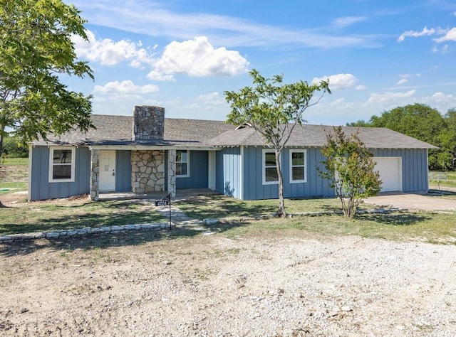 single story home with board and batten siding, a chimney, roof with shingles, dirt driveway, and an attached garage