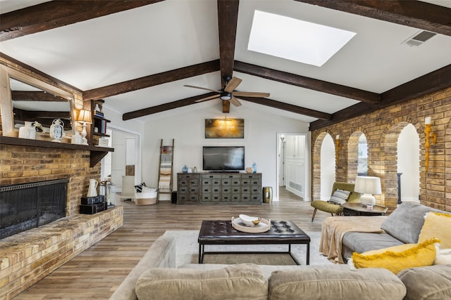 living room featuring visible vents, a brick fireplace, wood finished floors, and vaulted ceiling with skylight