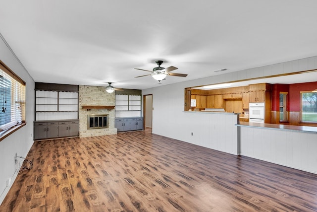 unfurnished living room featuring visible vents, a ceiling fan, a brick fireplace, and wood finished floors