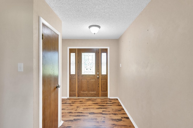 doorway to outside with a textured ceiling, baseboards, and wood finished floors