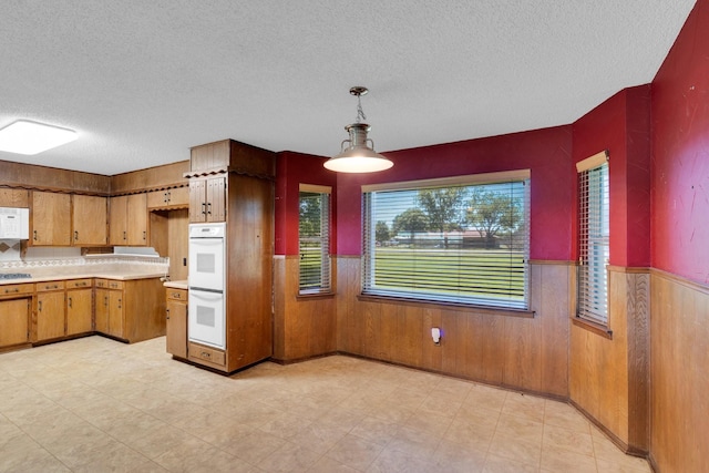 kitchen with light countertops, a textured ceiling, a wainscoted wall, and white appliances