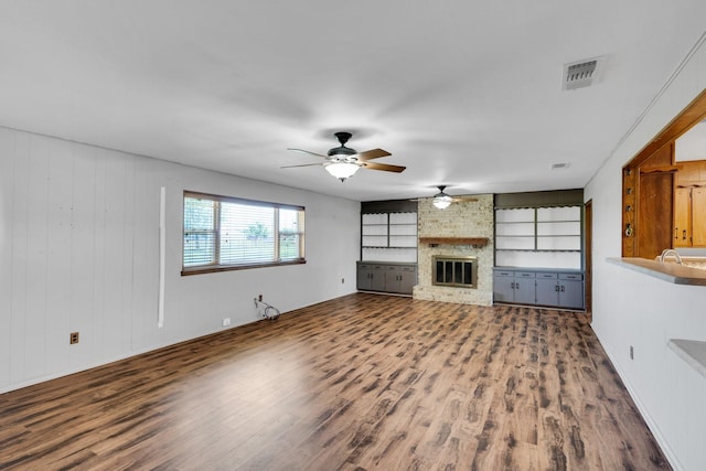 unfurnished living room featuring a brick fireplace, a ceiling fan, visible vents, and wood finished floors