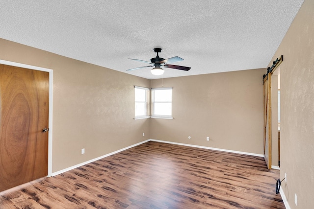 unfurnished bedroom with wood finished floors, baseboards, a barn door, a textured ceiling, and a ceiling fan