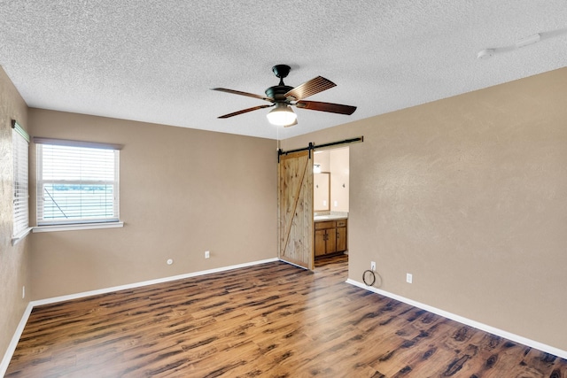 empty room with a ceiling fan, a textured ceiling, a barn door, and wood finished floors