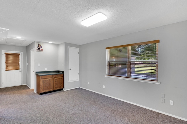 carpeted empty room with baseboards, attic access, and a textured ceiling