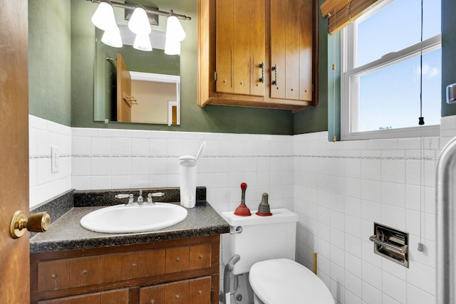 half bathroom featuring toilet, tile walls, wainscoting, and vanity