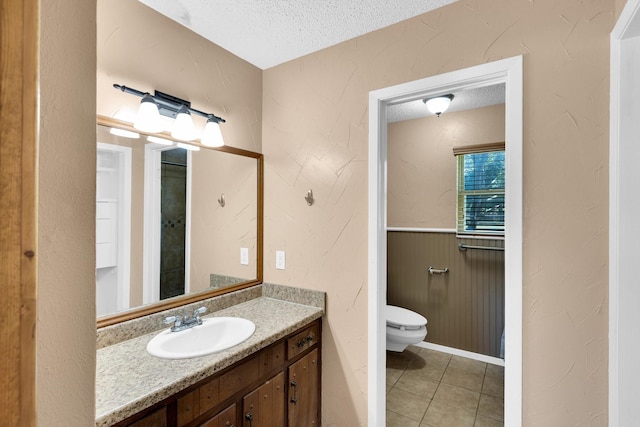 bathroom featuring wainscoting, vanity, toilet, a textured ceiling, and tile patterned floors