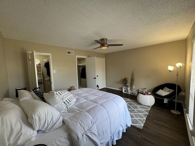 bedroom featuring a walk in closet, a textured ceiling, wood finished floors, visible vents, and a closet