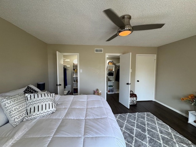 bedroom featuring visible vents, wood finished floors, ceiling fan, a walk in closet, and a textured ceiling