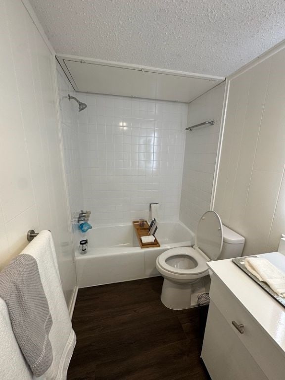 full bath with a textured ceiling, wood finished floors, toilet, and shower / bathing tub combination