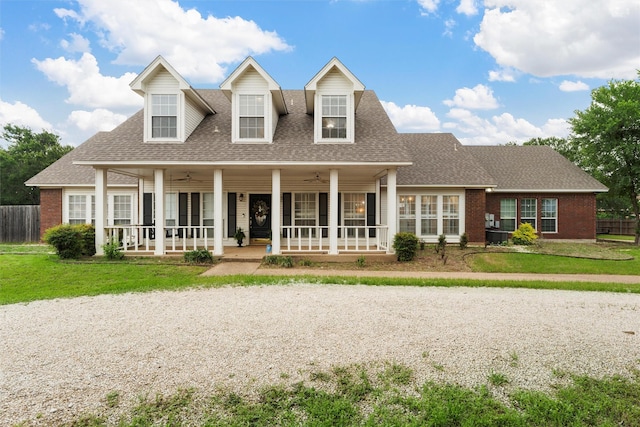 new england style home featuring a porch, a shingled roof, brick siding, and a front yard