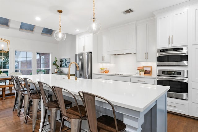 kitchen featuring a kitchen island with sink, light countertops, stainless steel appliances, backsplash, and visible vents