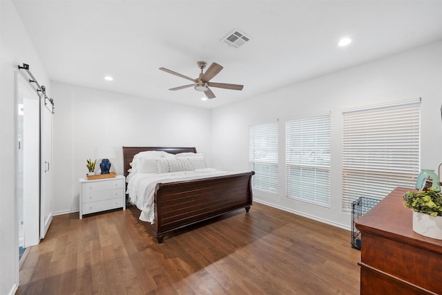 bedroom with wood finished floors, recessed lighting, a barn door, and visible vents
