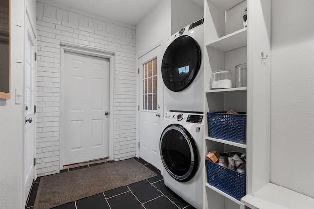 laundry room with laundry area, stacked washer / dryer, and dark tile patterned flooring