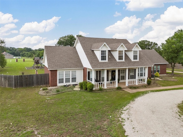 cape cod home with a porch, a front yard, roof with shingles, brick siding, and fence