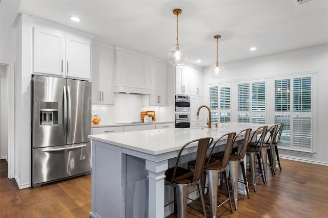 kitchen with light countertops, dark wood finished floors, an island with sink, stainless steel appliances, and backsplash