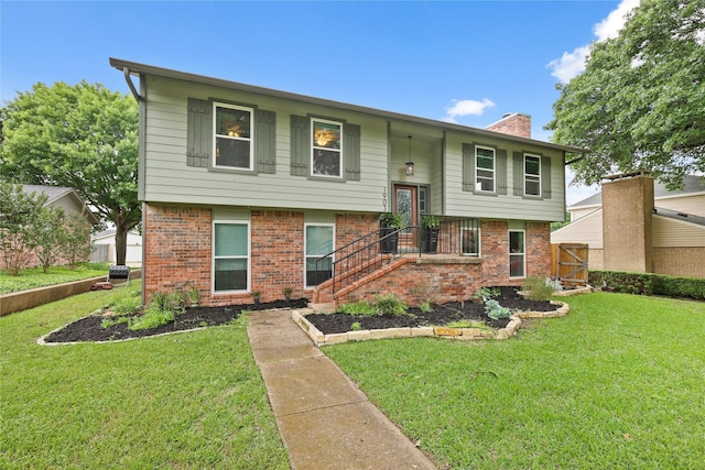 split foyer home featuring brick siding, fence, a chimney, and a front lawn