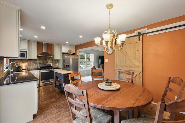 dining space featuring recessed lighting, dark wood finished floors, a barn door, and an inviting chandelier