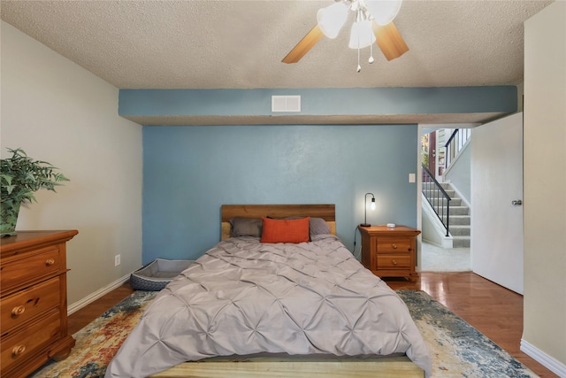 bedroom featuring a textured ceiling, a ceiling fan, baseboards, wood finished floors, and visible vents