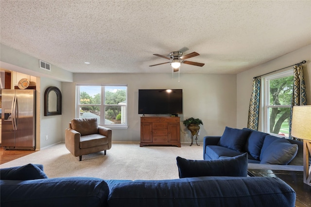 living room with baseboards, ceiling fan, a textured ceiling, and visible vents
