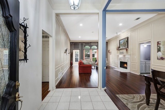 foyer entrance featuring crown molding, a decorative wall, light tile patterned floors, a tile fireplace, and visible vents