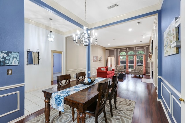 dining room with visible vents, dark wood finished floors, a notable chandelier, ornamental molding, and a decorative wall