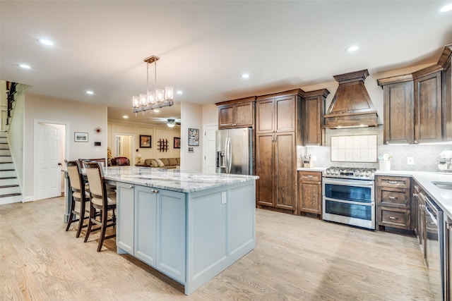 kitchen featuring a center island, tasteful backsplash, custom range hood, light wood finished floors, and appliances with stainless steel finishes
