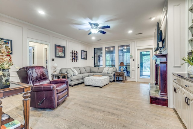 living area featuring ornamental molding, a decorative wall, a fireplace, ceiling fan, and light wood-type flooring