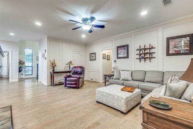 living area with crown molding, visible vents, a decorative wall, ceiling fan, and light wood finished floors