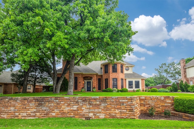 colonial inspired home featuring brick siding, a front lawn, and fence