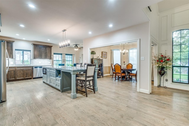 kitchen with appliances with stainless steel finishes, hanging light fixtures, light wood finished floors, a kitchen breakfast bar, and a center island