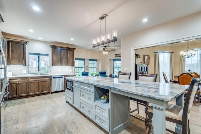 kitchen with black microwave, light wood finished floors, dishwasher, ceiling fan with notable chandelier, and a large island