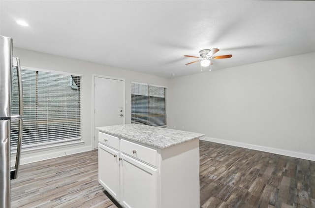 kitchen with wood finished floors, baseboards, ceiling fan, a center island, and white cabinetry