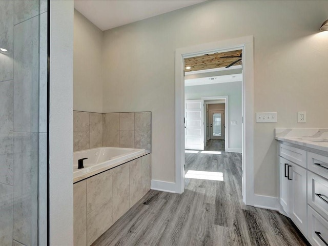full bathroom with baseboards, wood finished floors, a garden tub, and vanity