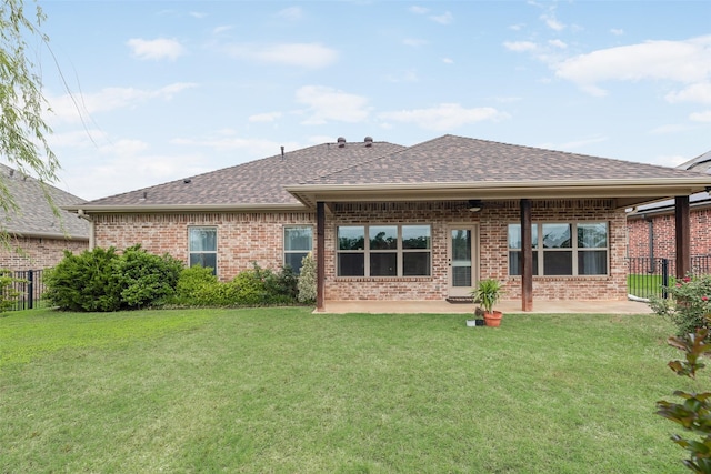back of property featuring fence, a shingled roof, brick siding, a lawn, and a patio